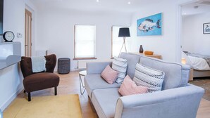 Een moderne woonkamer met een grijze bank, een bruine fauteuil, een salontafel en een schilderij aan de muur.