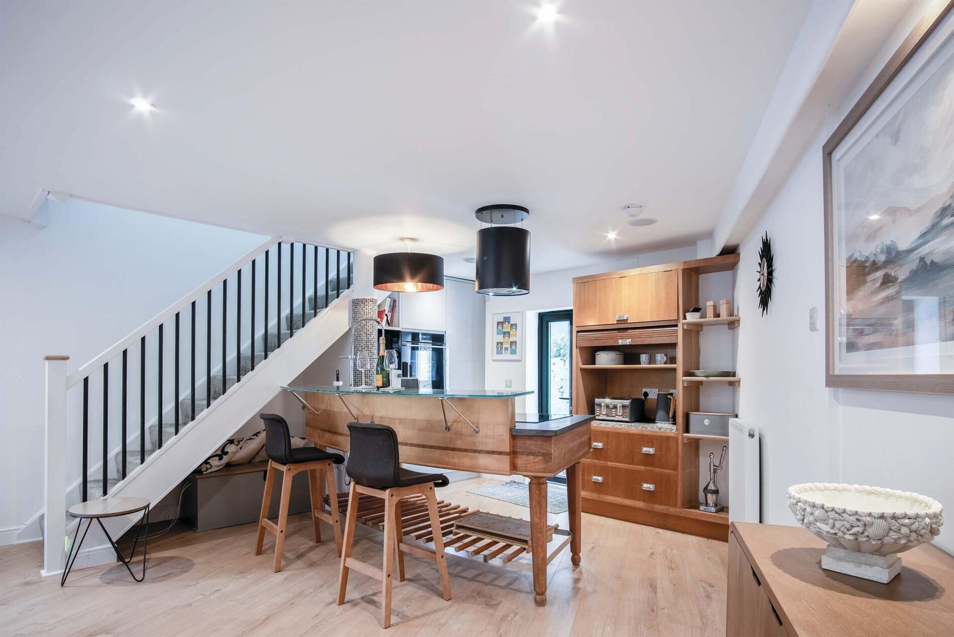 Una cocina moderna con barra de madera, una escalera y un comedor con taburetes.
