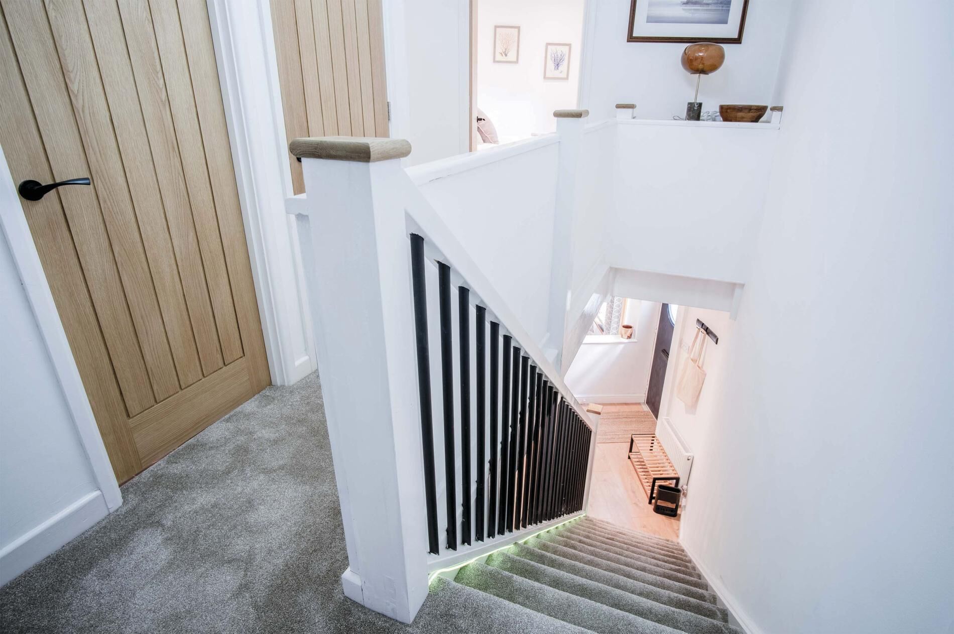 Un escalier avec une rampe blanche, des marches recouvertes de moquette et une porte en bois en haut.