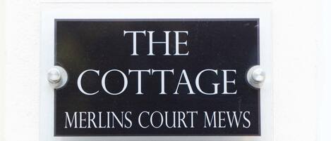 A sign with the text "THE COTTAGE MERLINS COURT MEWS".