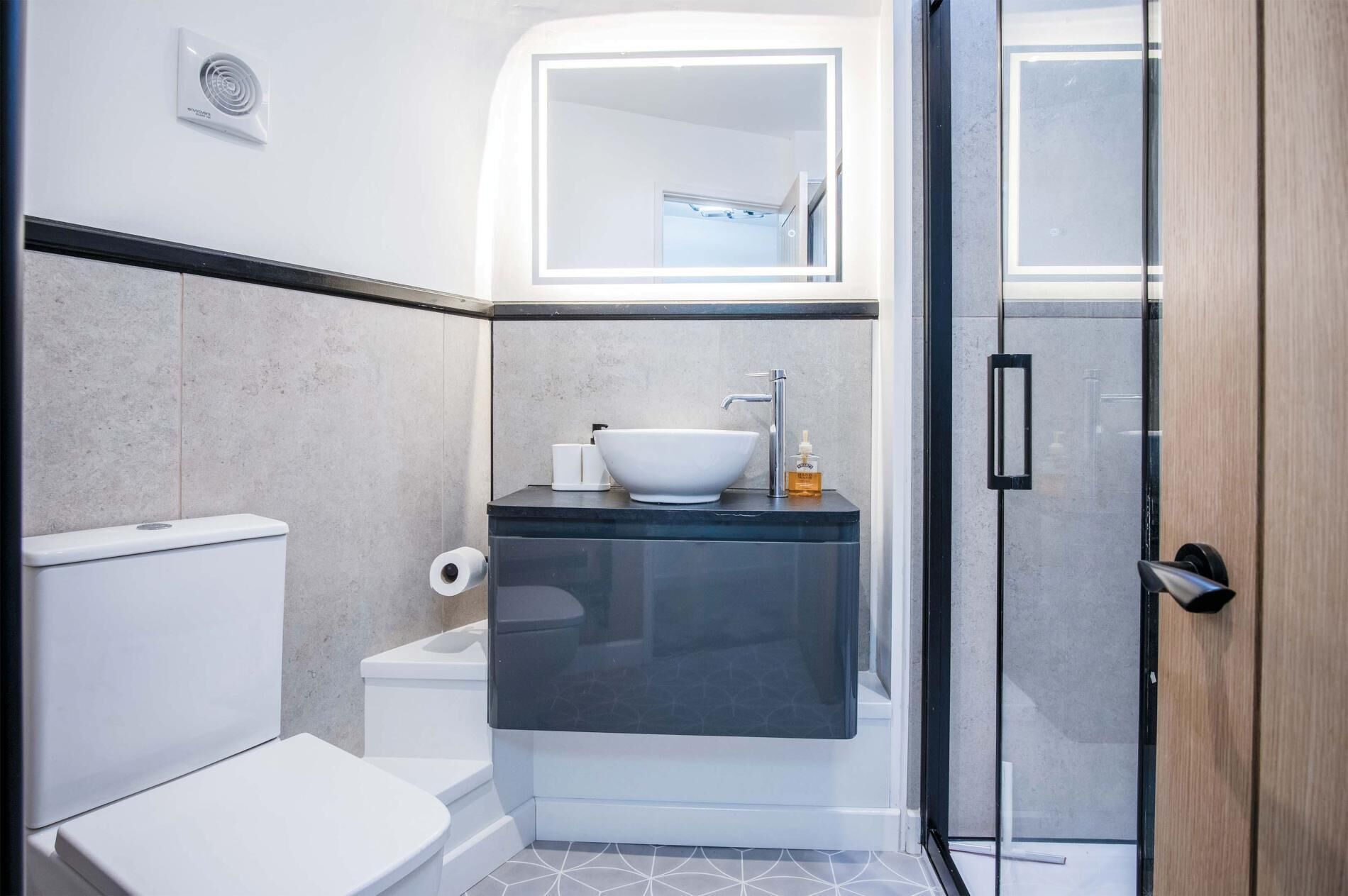 Een kleine badkamer met een wit toilet, een wastafel met een komwastafel en een douchecabine van glas.