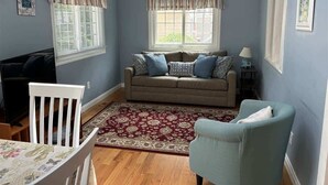 A living room with a sofa, two chairs, a table, and a window with curtains.