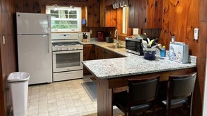 A kitchen with wooden paneling, a refrigerator, oven, microwave, granite countertop, and bar stools.