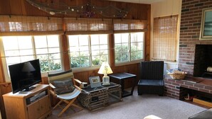 Ein gemütliches Wohnzimmer mit Fernseher, Holzmöbeln, Kamin und großen Fenstern.