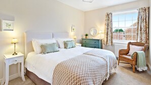 A bedroom with a large bed, two bedside tables, a dresser, a chair, and a window with curtains. - Moat Cottage - Luxury Country Cottage, Yorkshire Dales Views, Newby Hall Estate, Sleeps 4-5, Dog Friendly (Ripon)