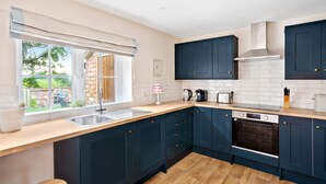 A modern kitchen with dark blue cabinets, a wooden countertop, a built-in oven, and a large window with a view of the outdoors. - Moat Cottage - Luxury Country Cottage, Yorkshire Dales Views, Newby Hall Estate, Sleeps 4-5, Dog Friendly (Ripon)