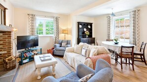 A cozy living room with a fireplace, a television, a sofa, a dining table, and a bookshelf. - Moat Cottage - Luxury Country Cottage, Yorkshire Dales Views, Newby Hall Estate, Sleeps 4-5, Dog Friendly (Ripon)