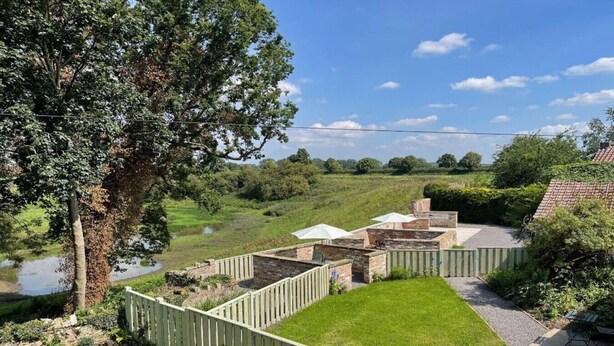 Ein Garten mit einer Ziegelterrasse, einem Holzzaun und Blick auf einen Teich.