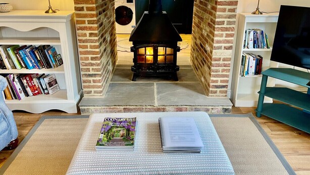 En hyggelig stue med en murstenspejs, bogreoler, et fjernsyn og et magasin på et sofabord.