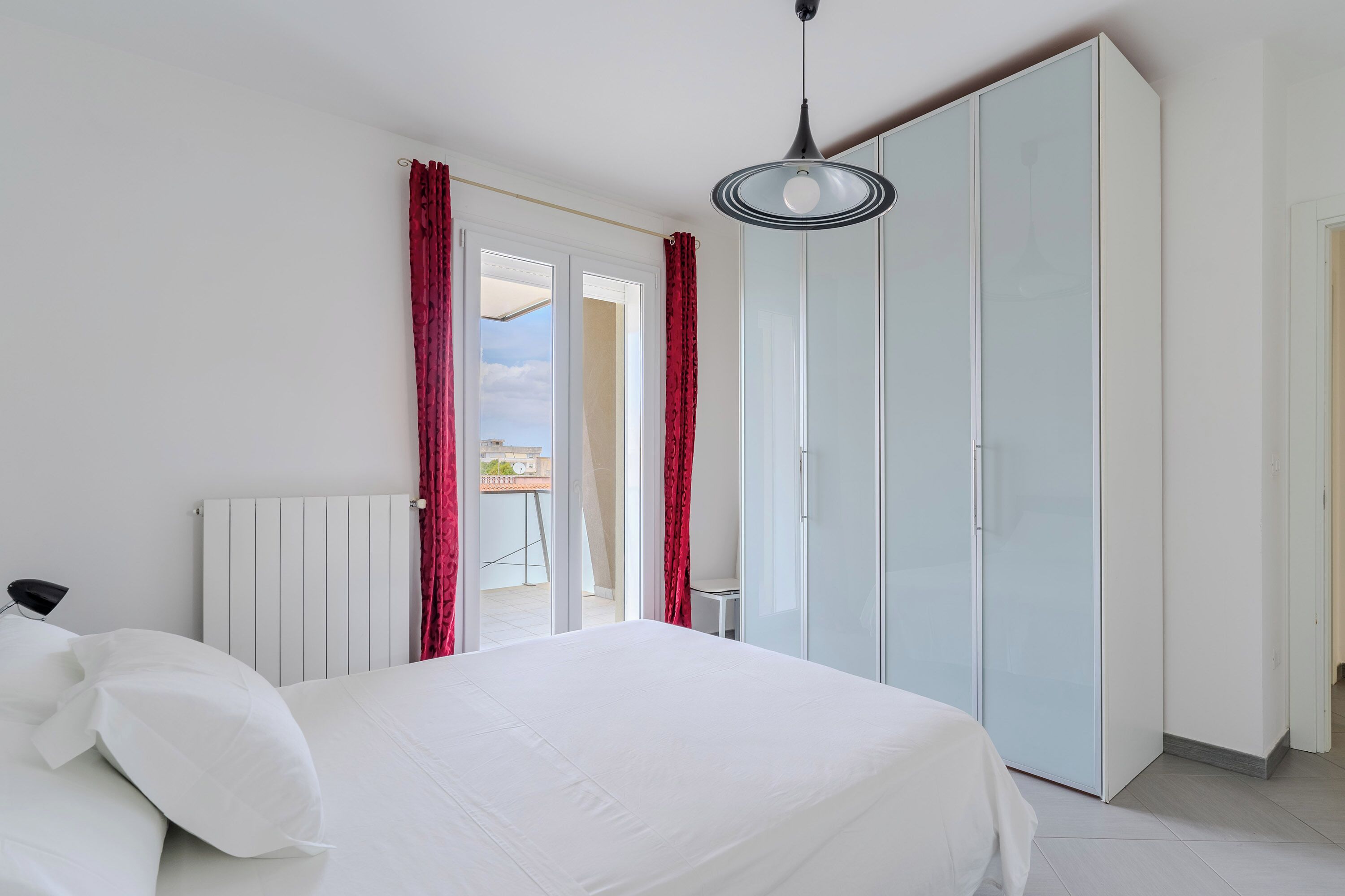 A bedroom with a bed, a radiator, a wardrobe, and a view through a door.
