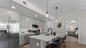 Uma cozinha moderna com eletrodomésticos de aço inoxidável, uma ilha central com banquetas e vista para o quarto vizinho.