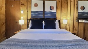 A wooden-paneled room with a bed, two wall-mounted lamps, and a door.