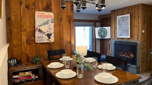 A dining area with a wooden table set for four, a fireplace, and a poster on the wall.