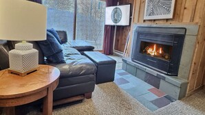 A cozy living room with a fireplace, a sofa, a coffee table, and a view of the outdoors.