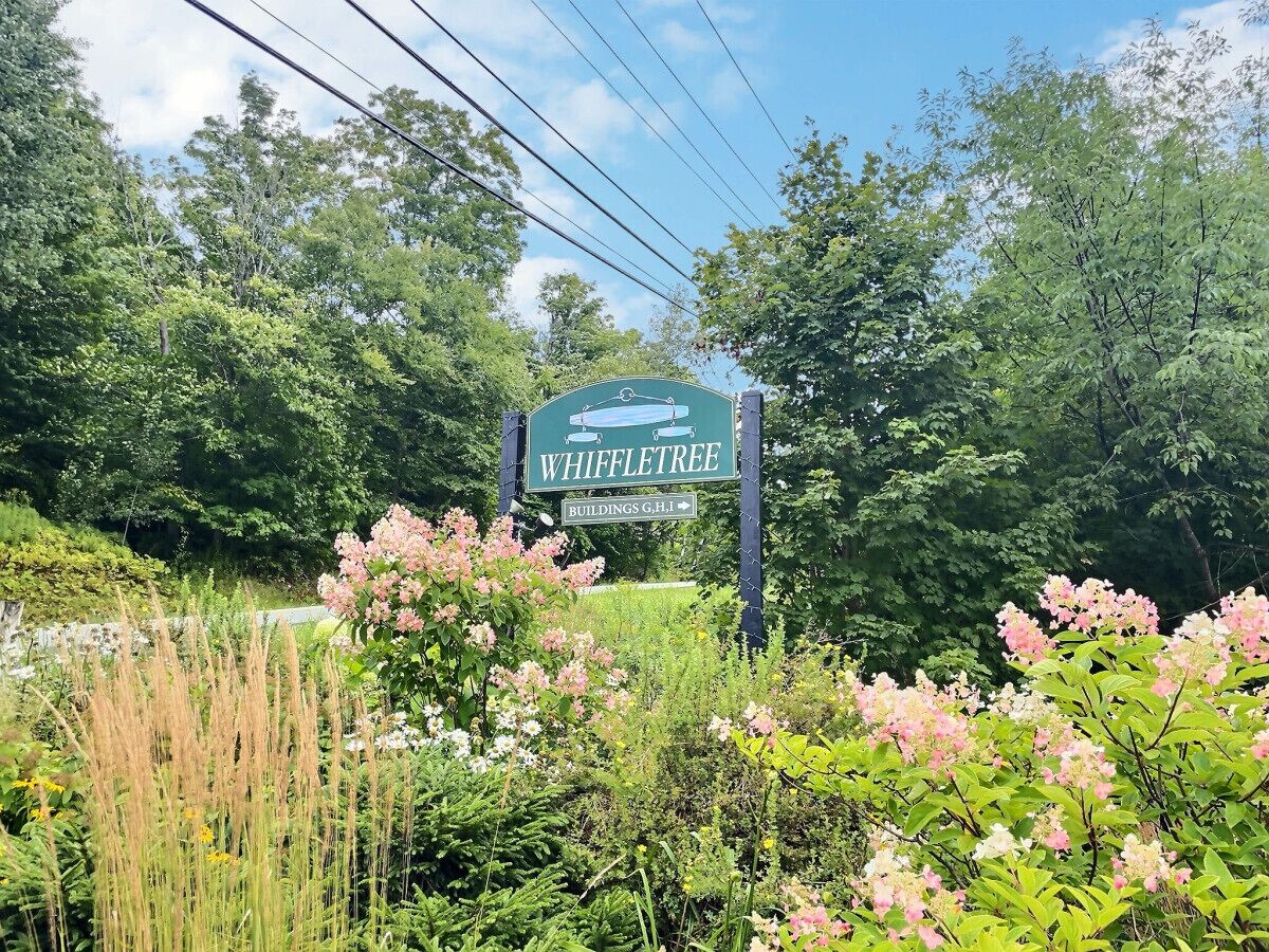 A sign for Whiffletree with a green background and white lettering, surrounded by lush greenery and flowering plants.