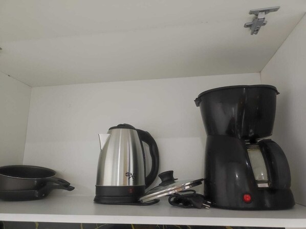Una cocina con tetera, cafetera y sartén sobre la encimera.