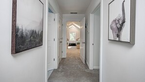 Un pasillo con cuadros en las paredes que conduce a un dormitorio con cama y ventana.