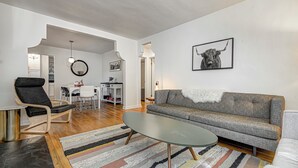 Una sala de estar moderna con un sofá gris, una silla negra, una mesa de centro de vidrio y un tapete a rayas.