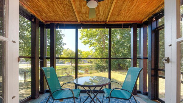 Un patio techado con mesa y sillas, ventanas amplias y vistas al exterior.