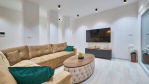 A modern living room with a beige sectional sofa, a round coffee table, and a flat-screen TV mounted on the wall. - Villa Adria Dream by Litto (Kastela)