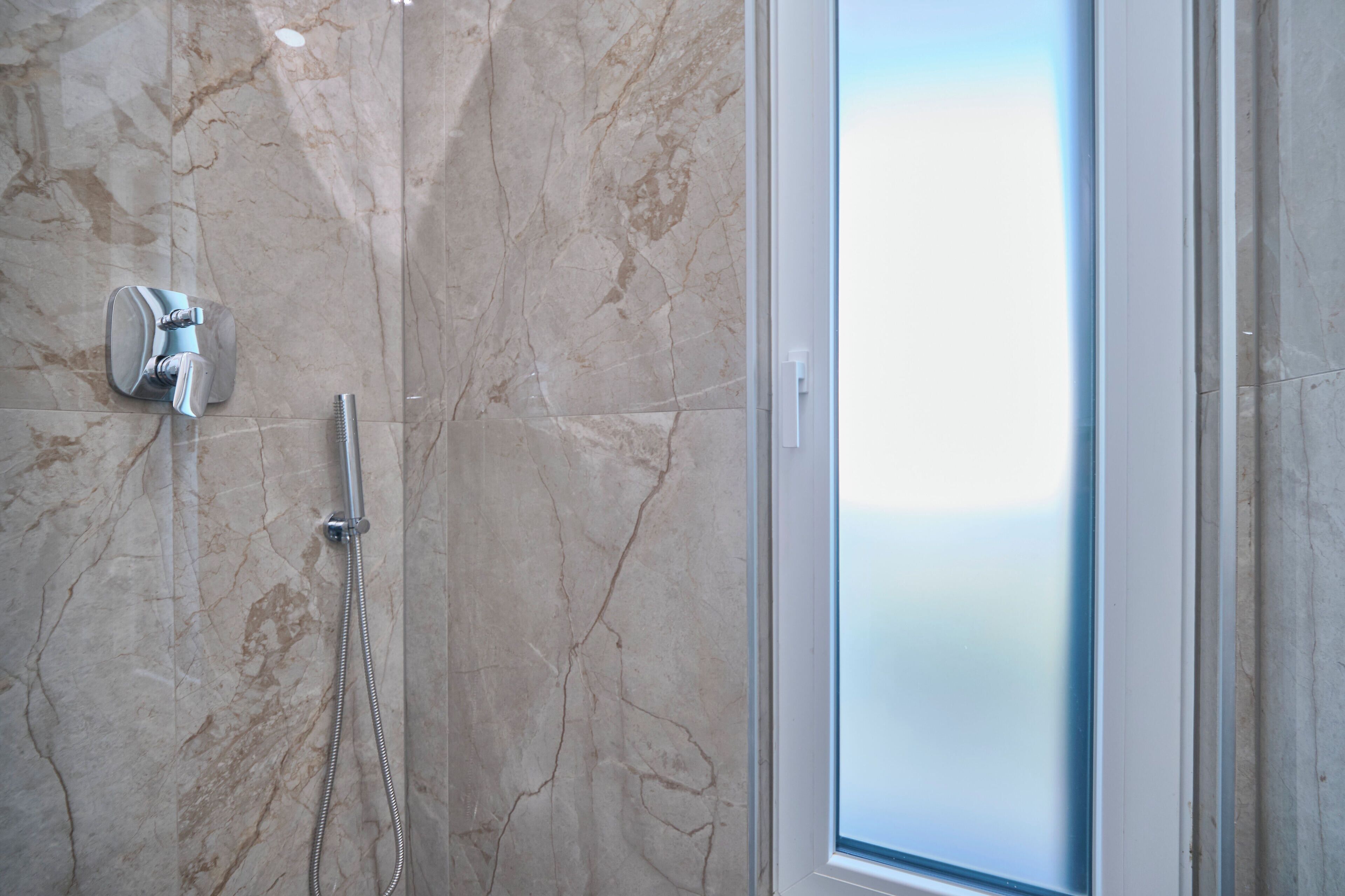 Un baño con ducha, puerta de cristal y paredes de mármol.