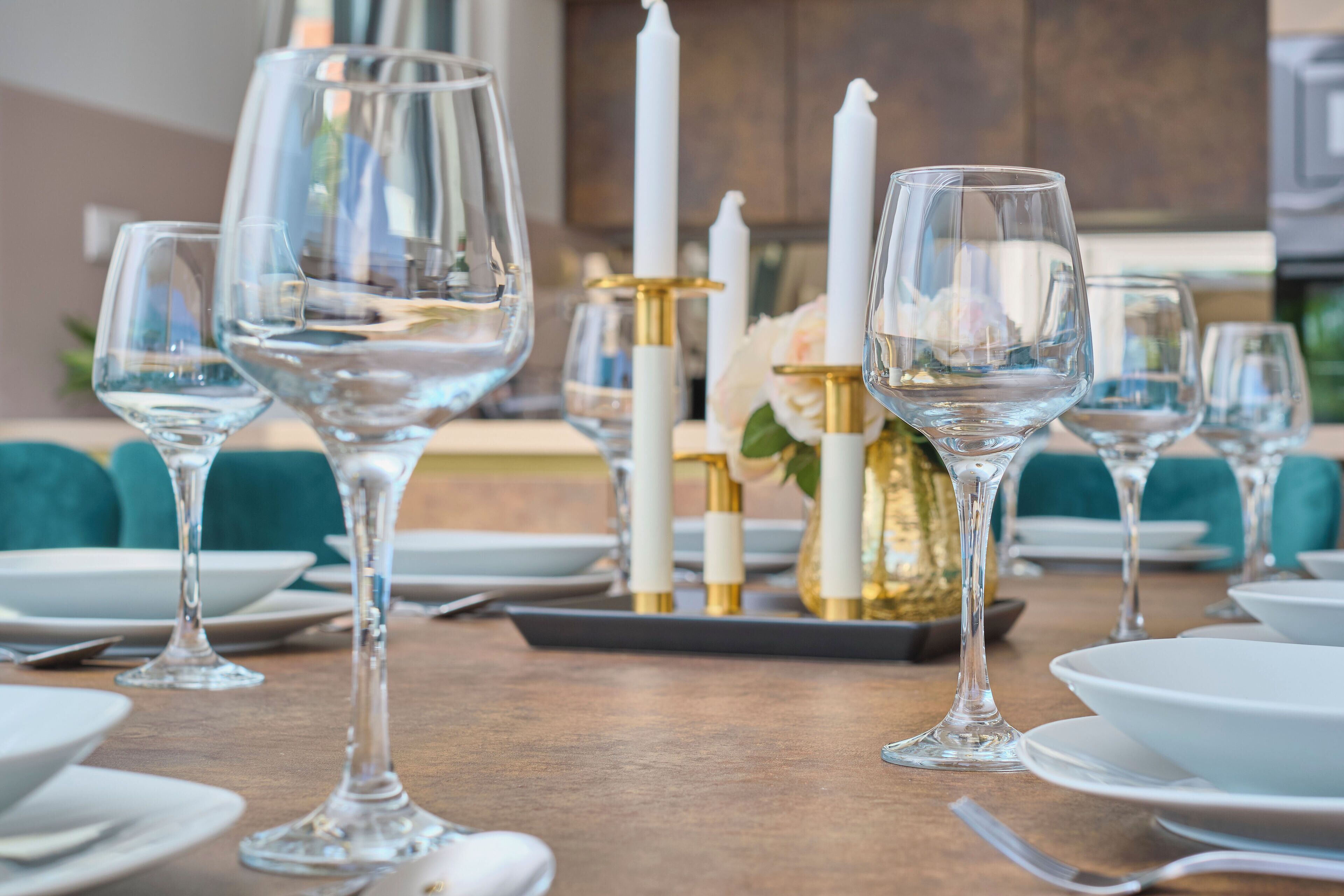 Une table à manger dressée avec des verres à vin transparents, des assiettes blanches et des chandeliers dorés.
