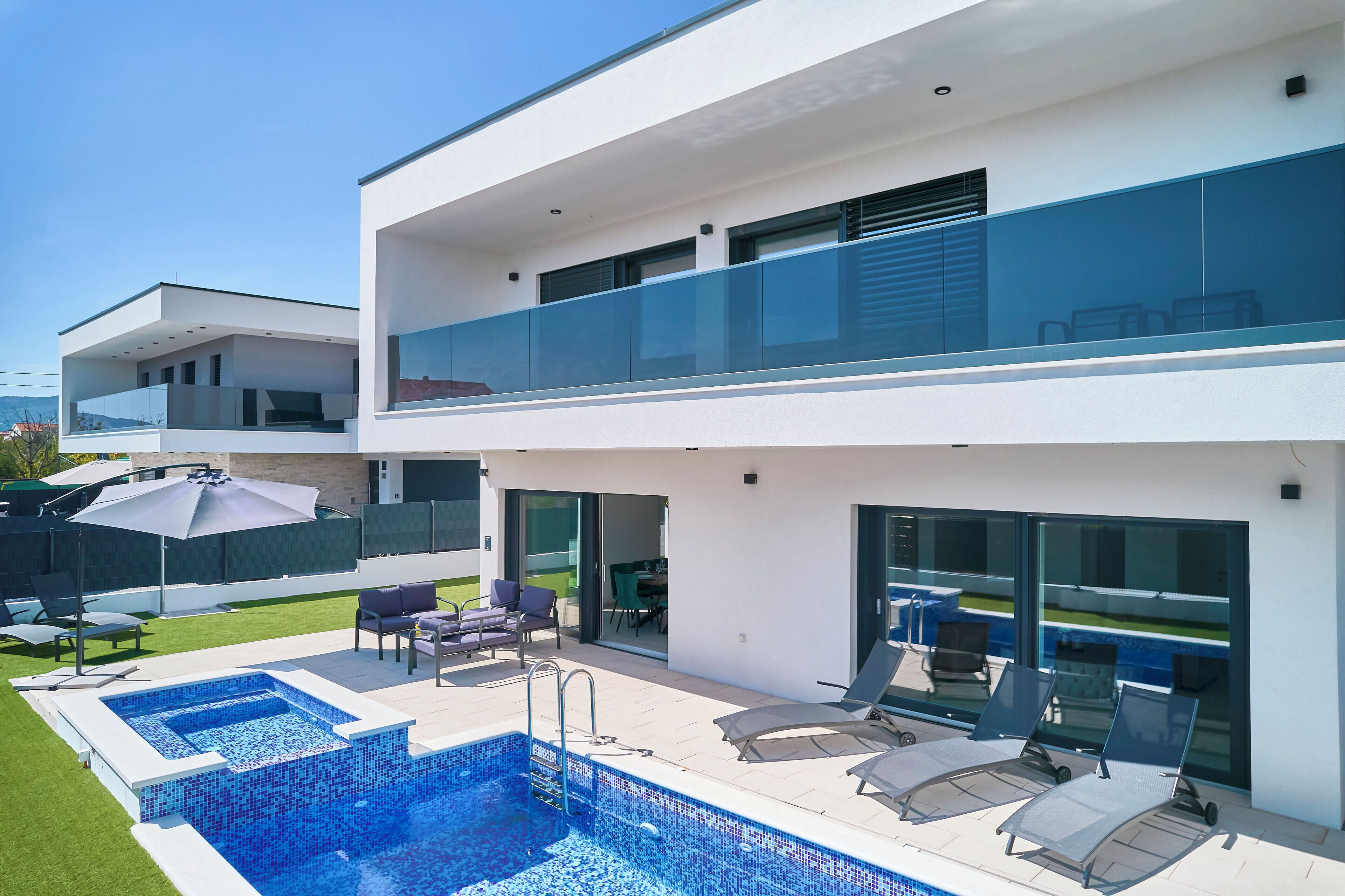 A modern two-story house with a swimming pool, outdoor seating, and a glass balcony.