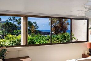 Une chambre dotée d’une grande fenêtre donnant sur un jardin tropical et l’océan.