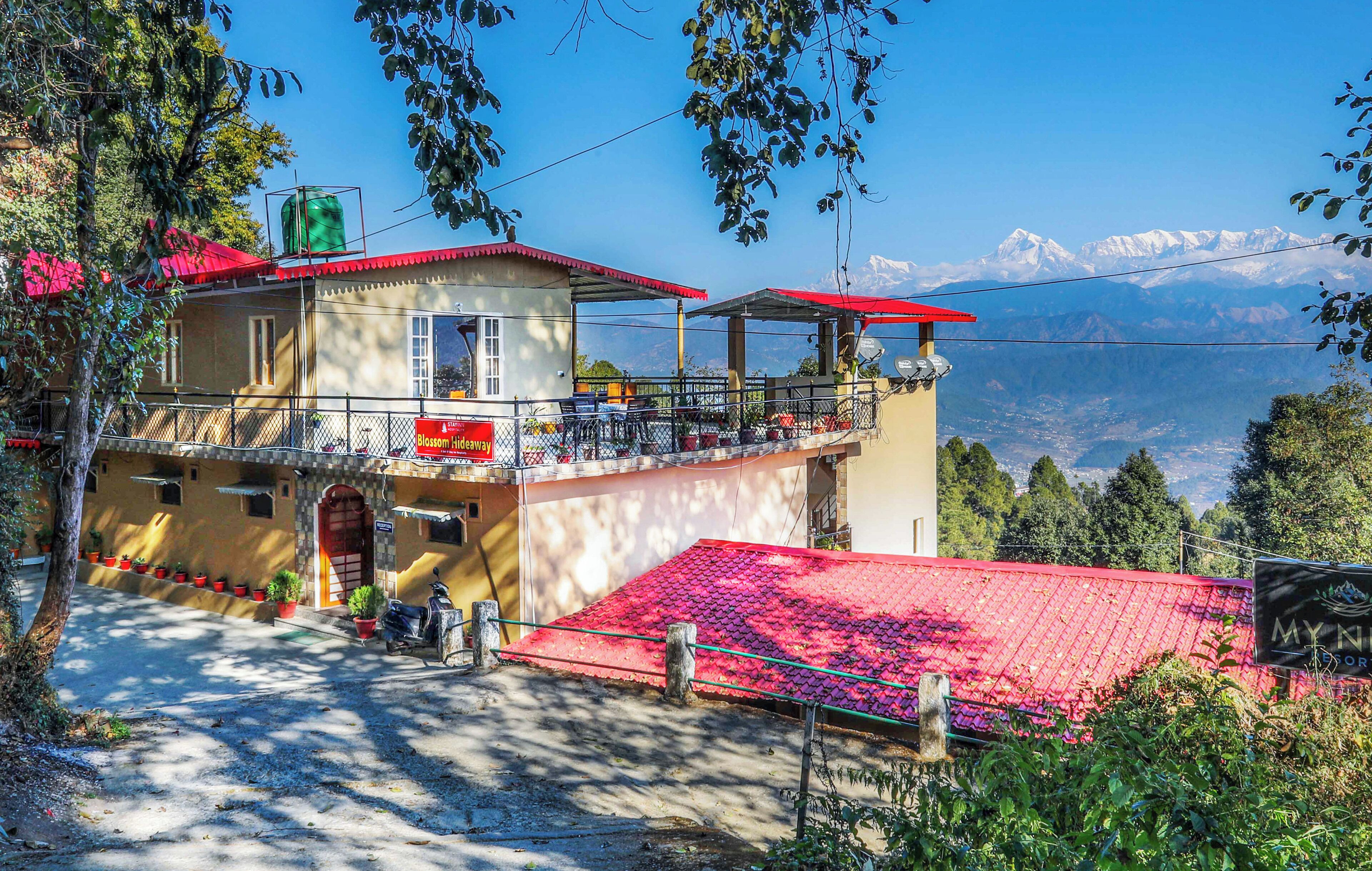 Un edificio de dos pisos con techo rojo y un balcón, con vistas a un paisaje montañoso.