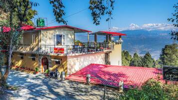 Un edificio de dos pisos con techo rojo y un balcón, con vistas a un paisaje montañoso.