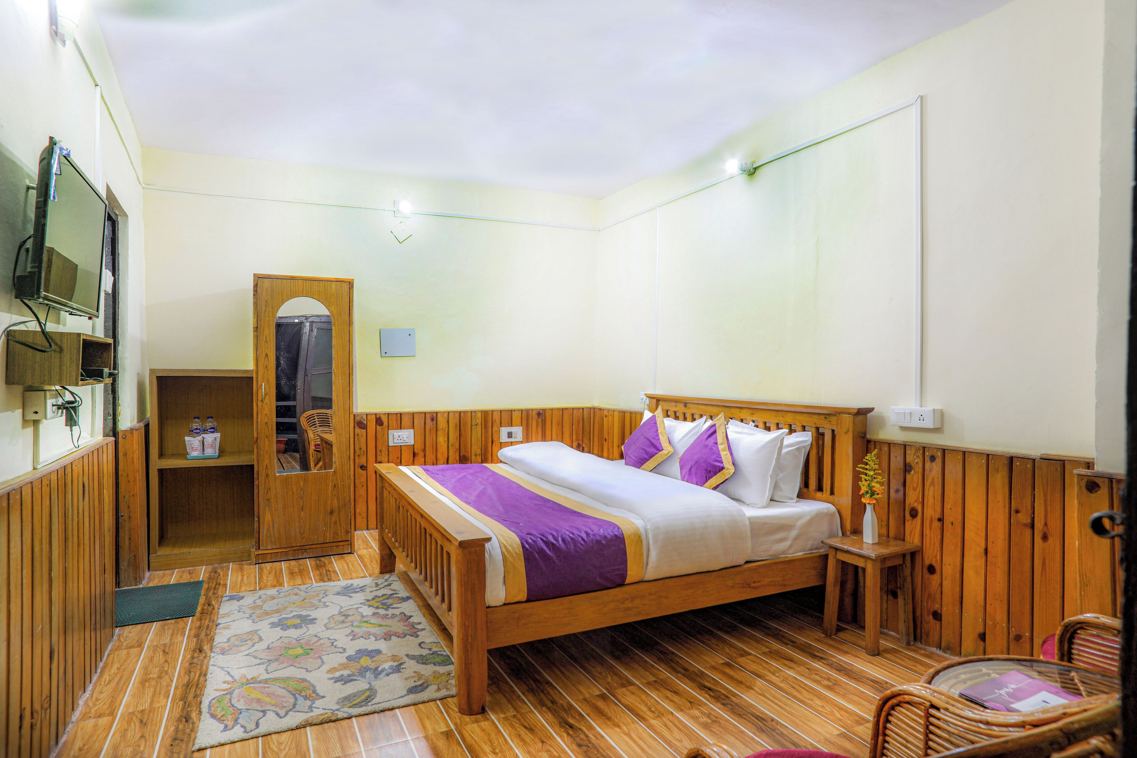 A wooden-framed bed with a purple and white bedspread, a small bedside table, and a chair.