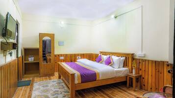 A wooden-framed bed with a purple and white bedspread, a small bedside table, and a chair.
