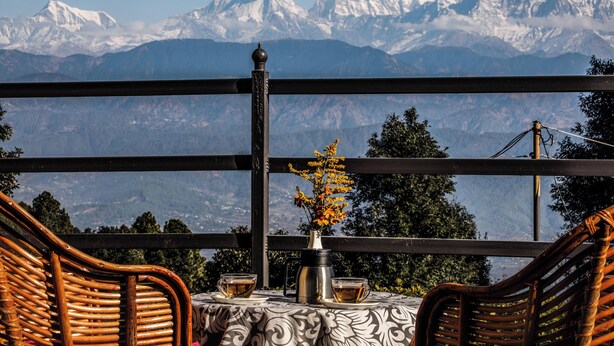 Una mesa con un florero y dos tazas, una silla de mimbre, y vistas de montañas nevadas.
