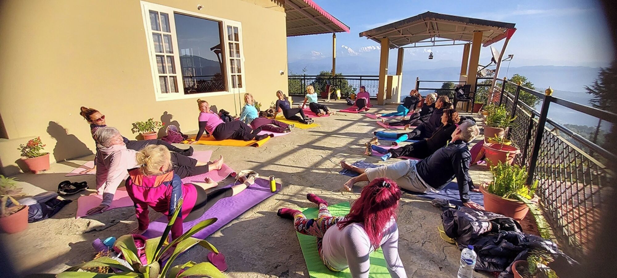 Een groep mensen doet aan yoga in de buitenlucht op een zonnige dag, met een prachtig uitzicht op de bergen op de achtergrond.