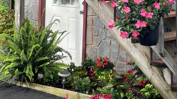 A wooden staircase with flower planters, a stone wall, and a door with a wreath. - Charming and immaculate 1-bedroom Suite/Apartment in Elizabethton  (Elizabethton)