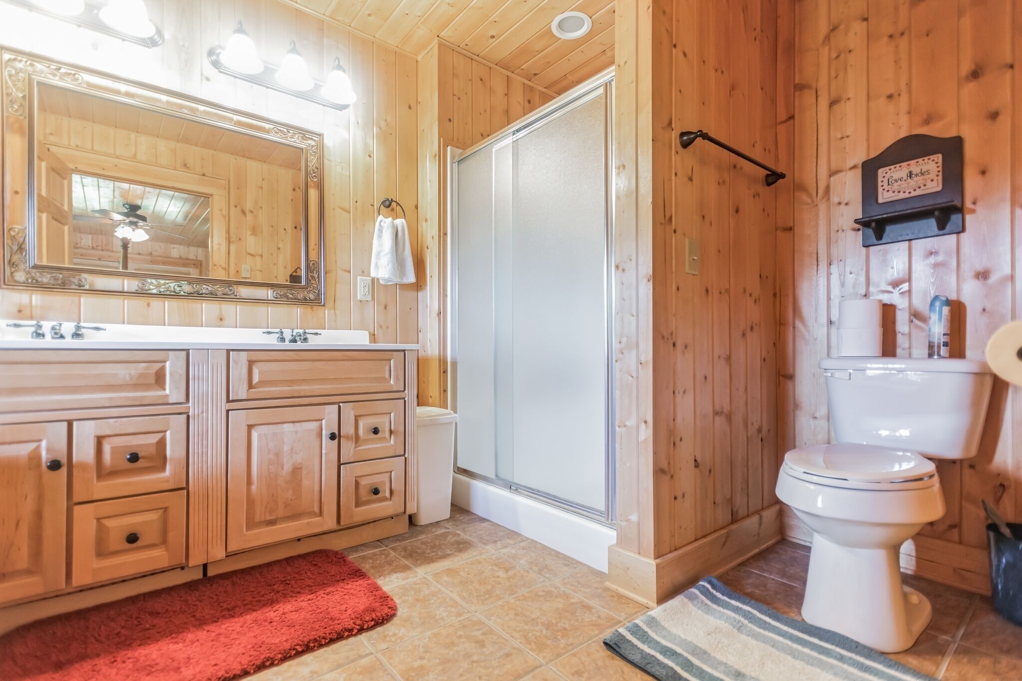 Een houten badkamer in een vakantiehuisje, met een grote spiegel, wastafel, toilet en douche.