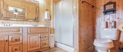 A wooden cabin bathroom with a large mirror, vanity, toilet, and shower.