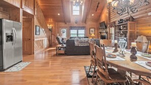 A wooden cabin interior with a dining area, kitchen, and living room.