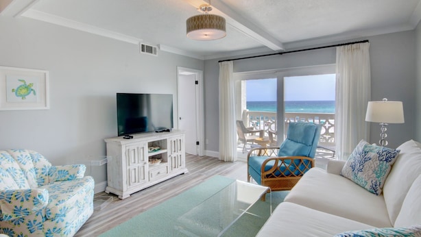 A living room with a TV, white furniture, a view of the ocean, and a balcony with chairs. - 331 El Matador 2 Bedroom Home by RedAwning (Fort Walton Beach)