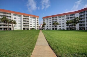 Um hotel moderno com um caminho central que leva a um edifício com várias varandas e um telhado vermelho.