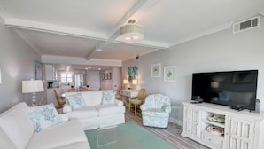 A modern living room with a white sofa, a glass coffee table, a TV on a white cabinet, and a dining area in the background. - 331 El Matador 2 Bedroom Home by RedAwning (Fort Walton Beach)