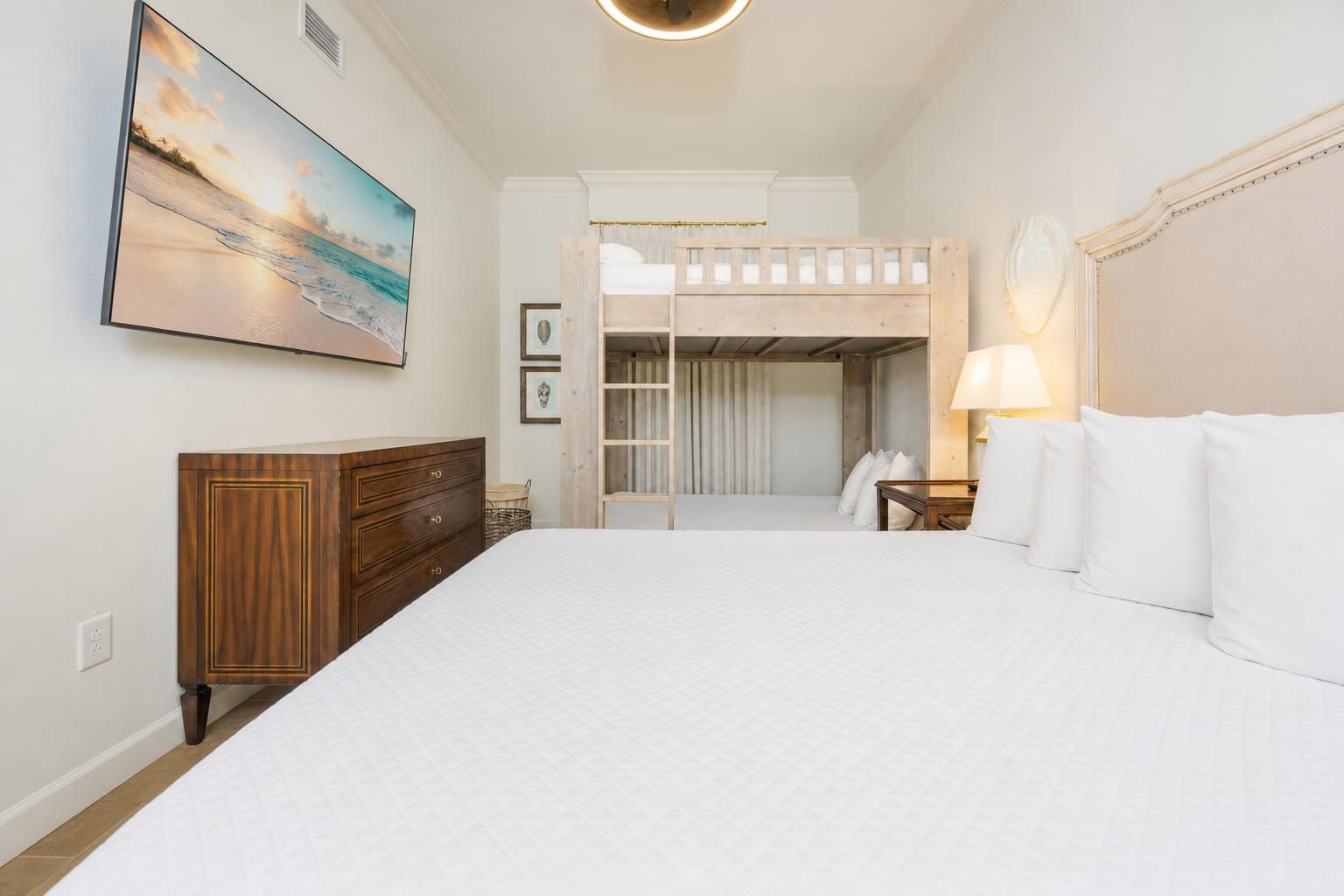 Een hotelkamer met een groot bed, een houten dressoir, een schilderij van een strandgezicht en een uitzicht op een balkon.