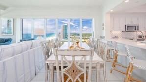 A dining area with a view of the ocean, white furniture, and a kitchen with white cabinets. - Phoenix Orange Beach Ii 1701 4 Bedroom Condo by RedAwning (Orange Beach)