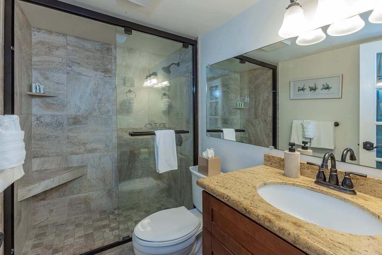 A modern bathroom with a glass-enclosed shower, a white toilet, a granite countertop sink, and a large mirror.