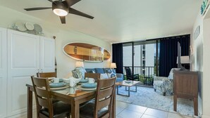 A dining area with a table set for four, a ceiling fan, and a view of the outdoors through a sliding glass door.