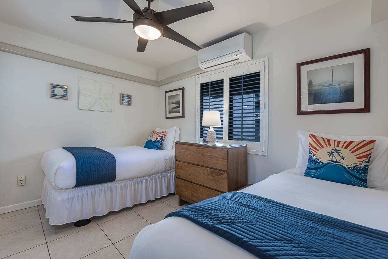 A bedroom with two beds, a ceiling fan, an air conditioning unit, a dresser, and a window with blinds.