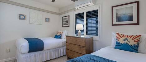 A bedroom with two beds, a ceiling fan, an air conditioning unit, a dresser, and a window with blinds.
