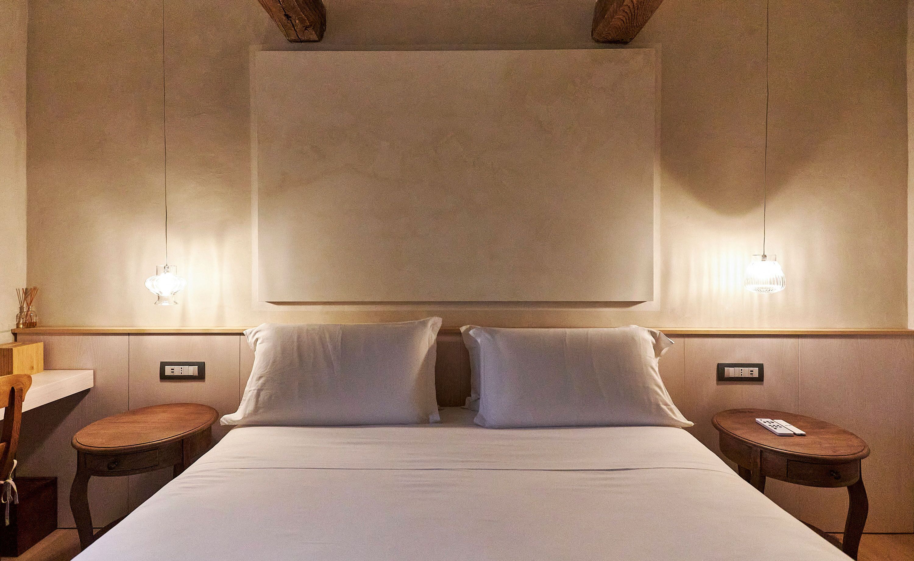 Una habitación de hotel con una cama grande, dos mesitas de noche, un escritorio y lámparas de pared.