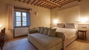 Ein Schlafzimmer mit einem großen Bett, einer Couch, einem Fenster mit Vorhängen, einem Nachttisch und einer Lampe.