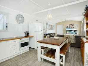 A compact kitchen with white cabinetry, a wooden dining table, and a bench.